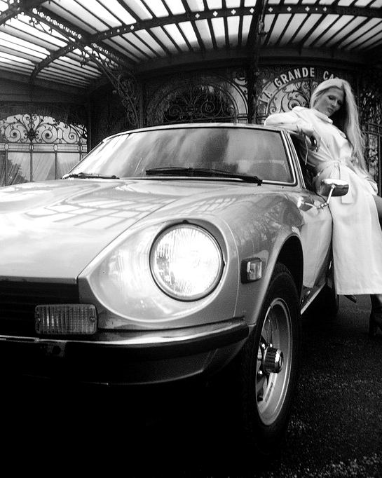 Woman in a fur coat beside a 1978 sports car under a glass canopy